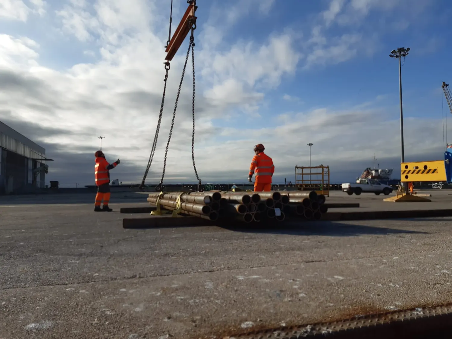 A crane lifting a bundle of steel from the quay while two men in overalls watch