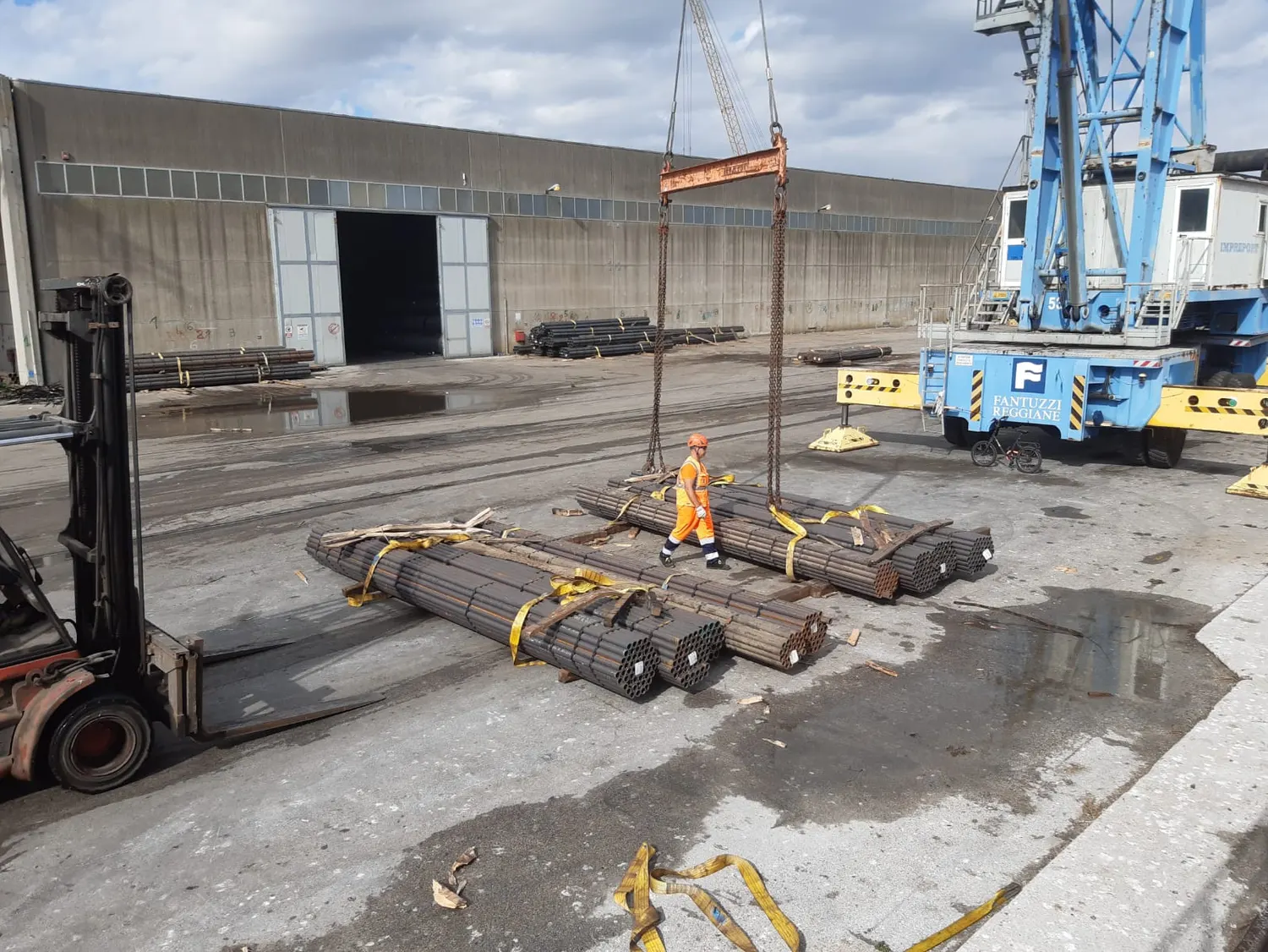 Forklift and crane handling bundles of steel on a quay